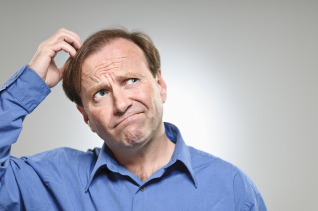 A mature man in his 50's scratching his head while making a decision.